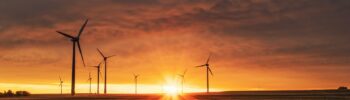 "Západ slunce nad větrnými elektrárnami symbolizuje udržitelný rozvoj a integraci obnovitelných zdrojů energie v rámci místní energetické koncepce a akčního plánu pro udržitelnou energii a klima. Obrázek zdůrazňuje důležitost plánování, které podporuje energetickou soběstačnost, snižuje uhlíkové emise a zajišťuje harmonii mezi technologií a přírodou.